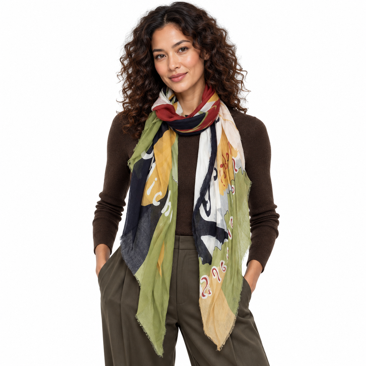 A woman with curly brown hair models a lightweight, multicolored patterned scarf wrapped around her neck, paired with a brown long-sleeve top and olive green pants against a plain white background.